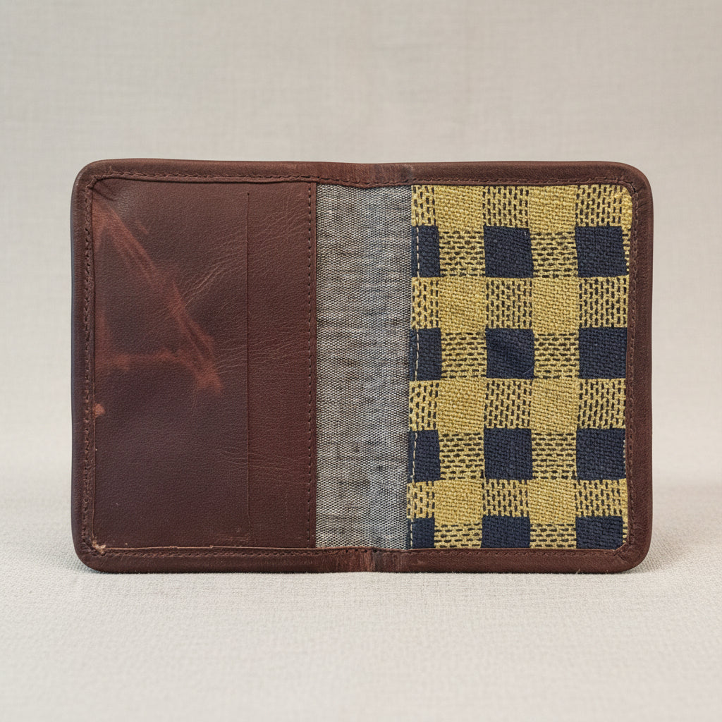 A handmade Checks - Mustard and indigo - block printed passport holder with leather trim - open shown open, featuring a dark brown leather interior, a gray fabric divider, and a mustard and navy blue checkered patterned panel on the right side.