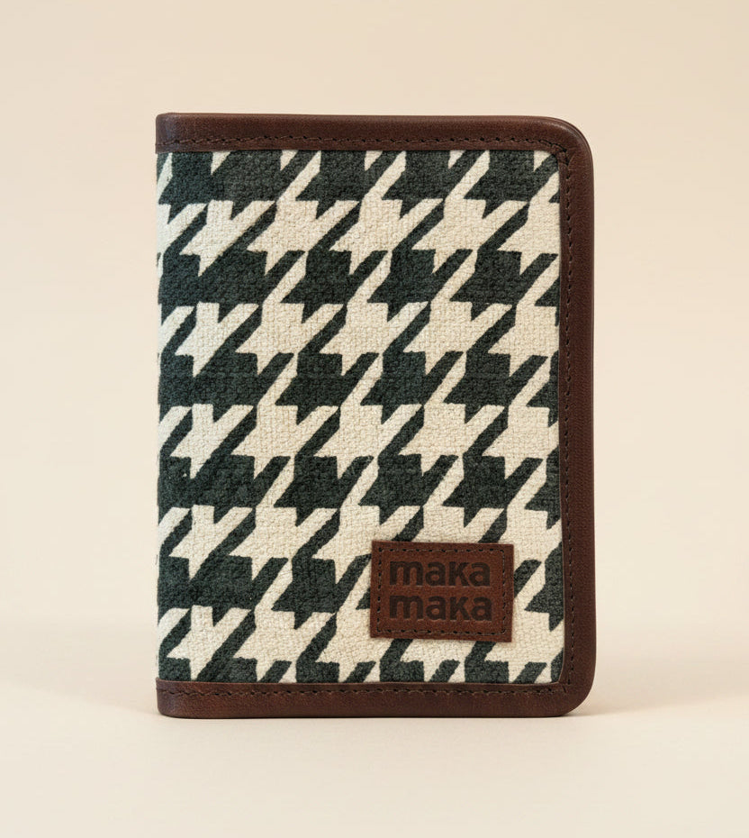 A passport holder with a black and off-white houndstooth pattern, brown leather trim burlap-canvas