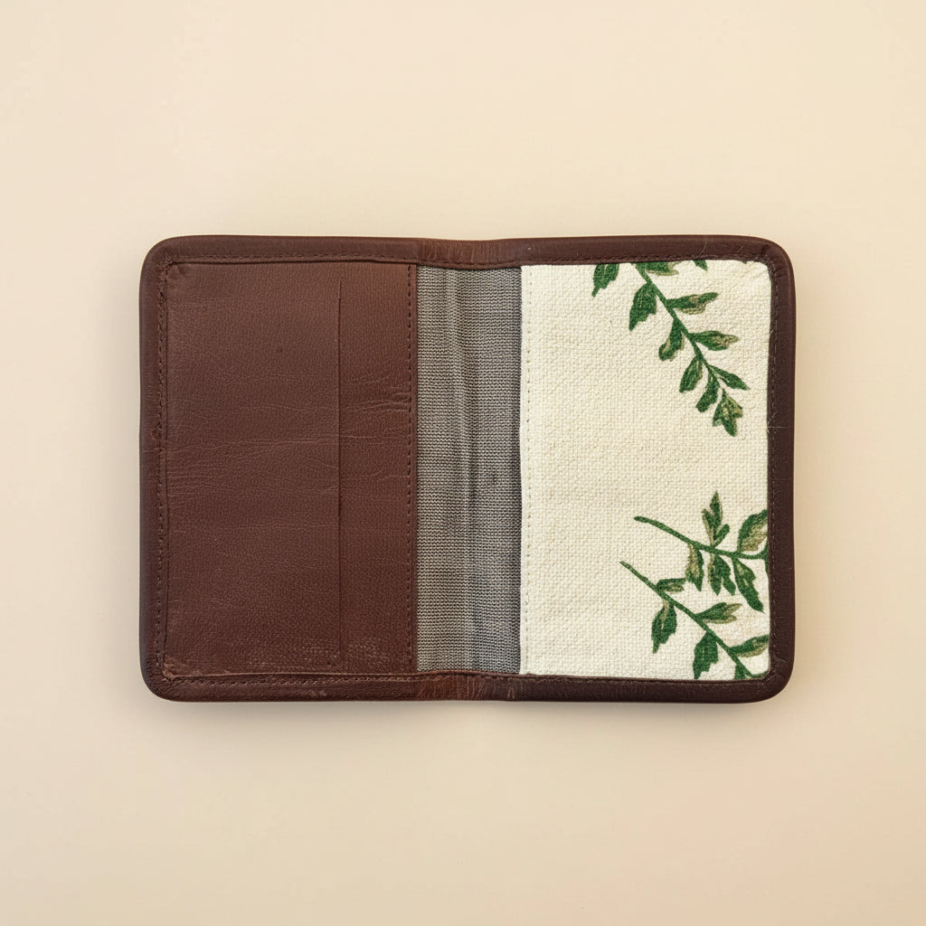 An open passport holder with a brown leather interior, panel with a botanical block printed burlap,  travel accessory