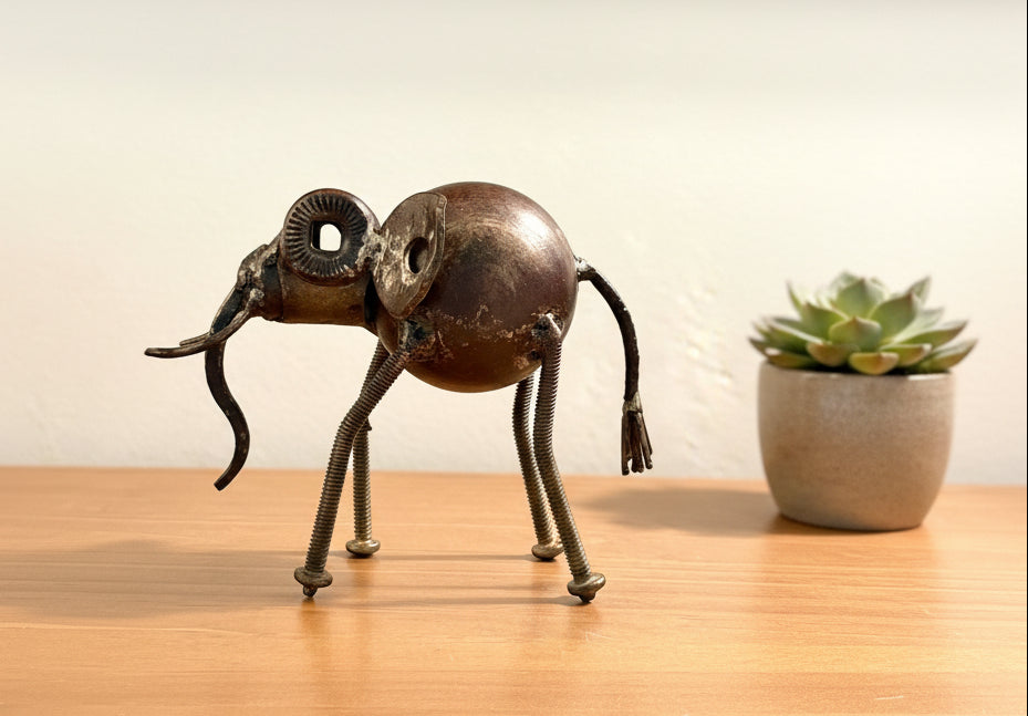A handmade metal elephant figurine crafted from scrap parts, including a spherical body, coiled spring legs, and a spiral trunk, lowered