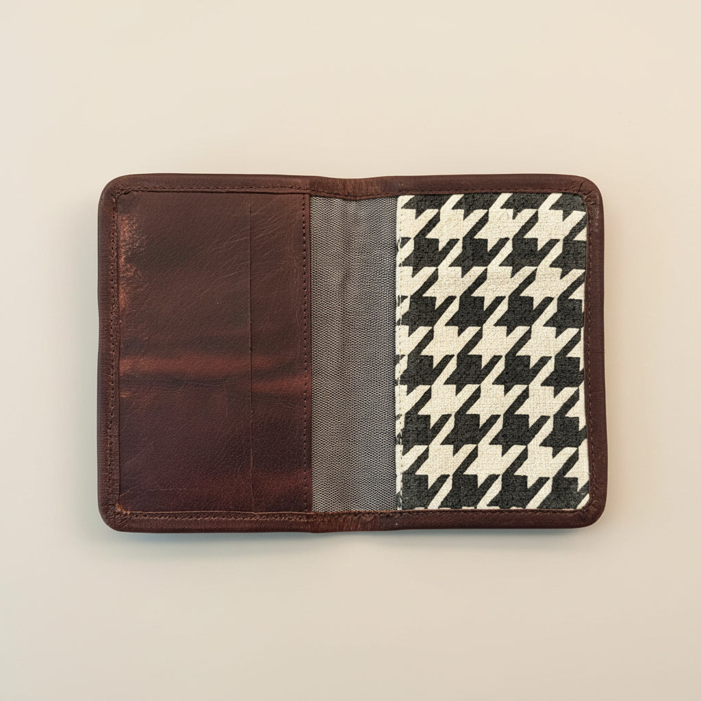 A Houndstooth block printed burlap-canvas passport holder with leather trim shown open. The interior features a solid dark brown leather section on the left, a gray cotton panel in the middle, and a black and cream houndstooth patterned panel on the right.